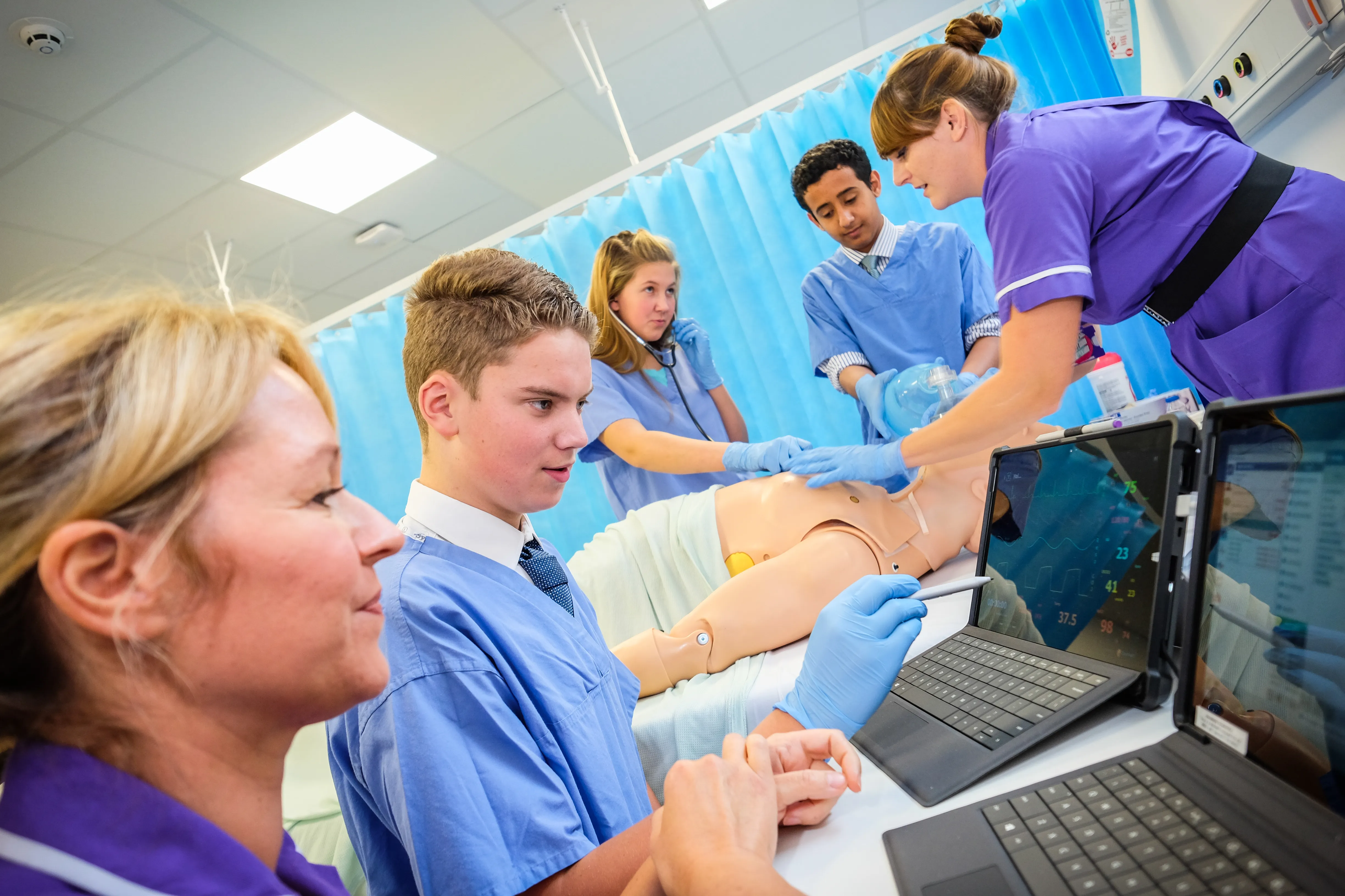Students in scrubs training on a patient simulator under supervision