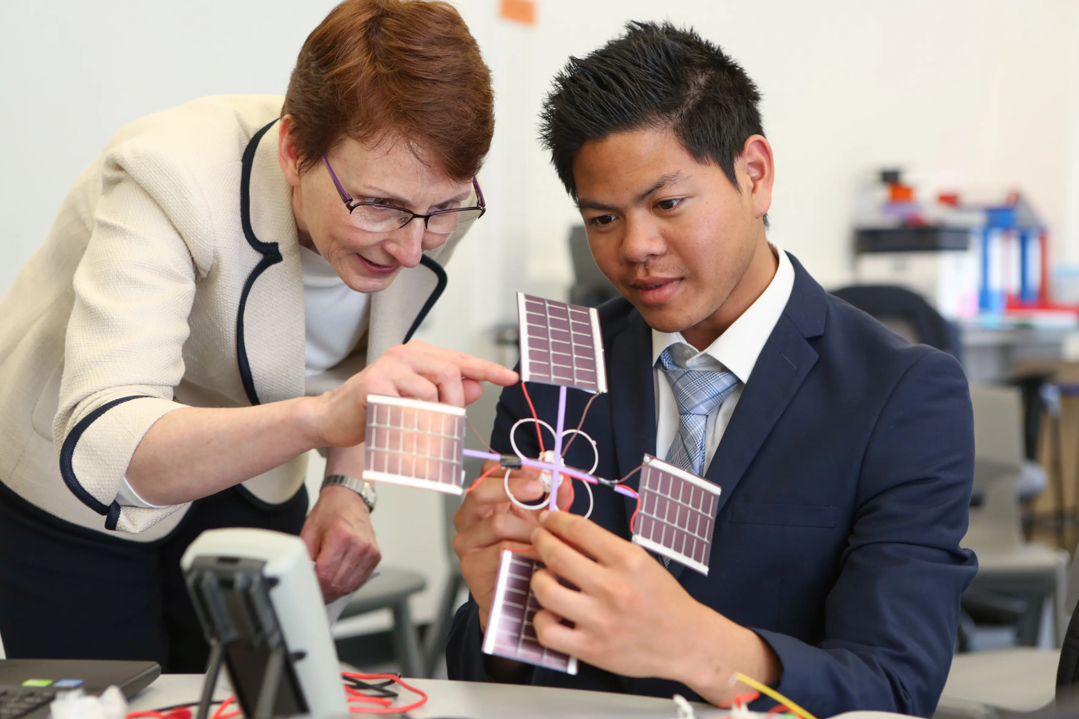 Teacher and student examining a solar panel model in an engineering classroom