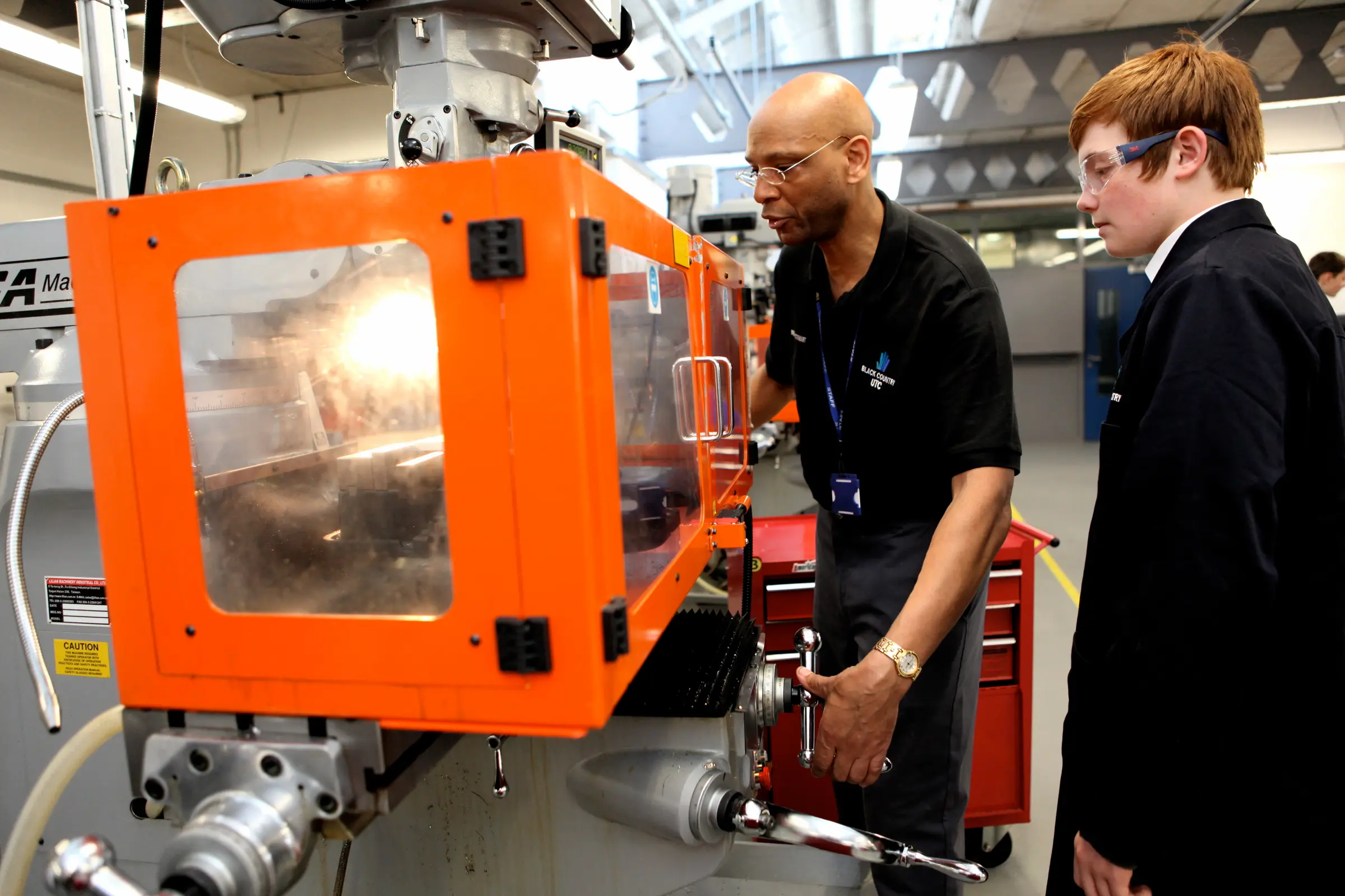 Teacher and student operating an injection moulding machine in a workshop